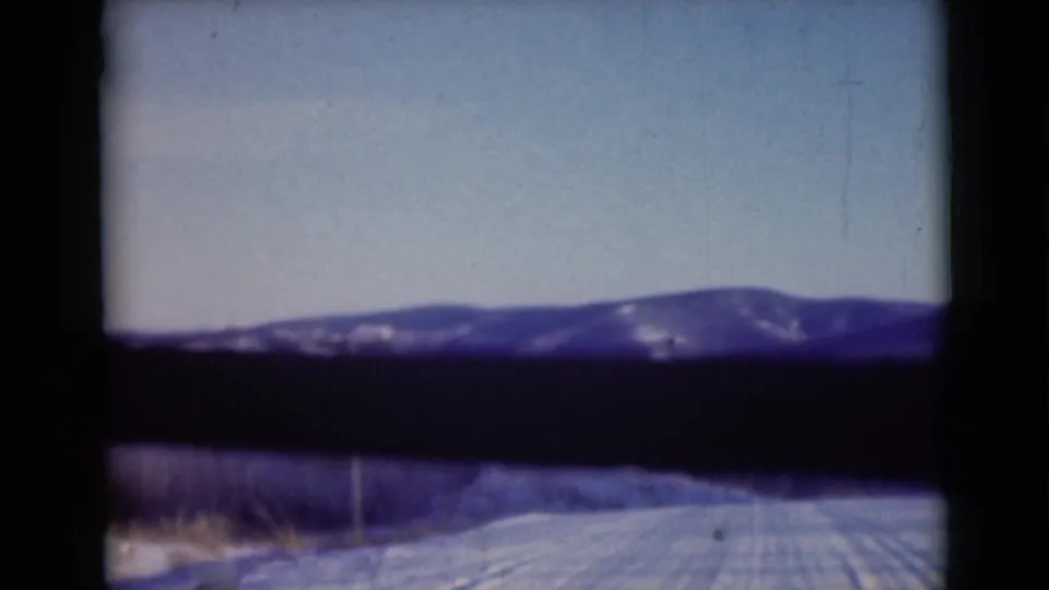 1946 Alaska home-movie frame showing a snowy road and roadside brush leading toward distant winter mountains.