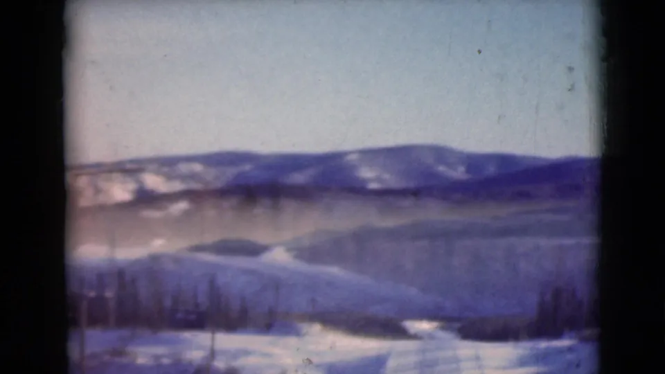 1946 Alaska winter landscape with a pale road or snowfield in the foreground, evergreen trees, and blue-toned mountain ridges beyond.