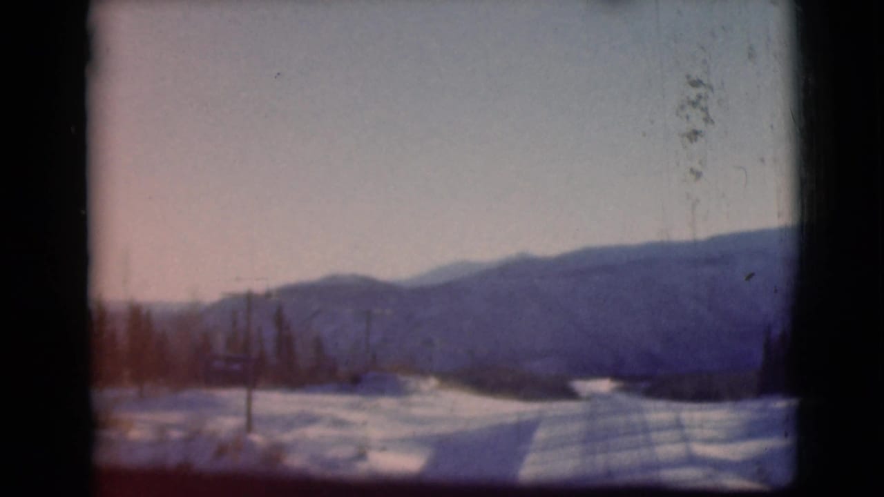 Snowy road or field leading toward distant blue mountains under a pale sky.