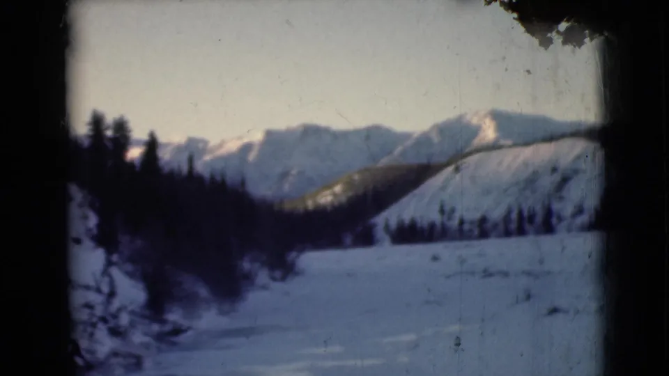 1946 Alaska 8mm frame looking across a snowy valley toward dark evergreens and snow-dusted mountains.
