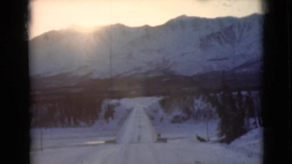 1946 Alaska 8mm frame showing a straight snow road, low sun over mountains, and dark trees along the route.