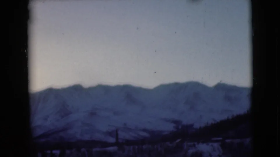 1946 Alaska 8mm still showing a blue-toned snowy mountain horizon with dark frame edges and indistinct foreground forms.