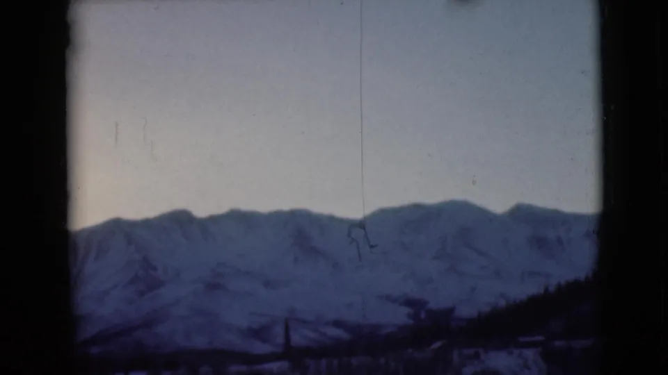 1946 Alaska 8mm frame of a snow-covered mountain ridge, pale sky, dark window-like borders, and small surface scratches.