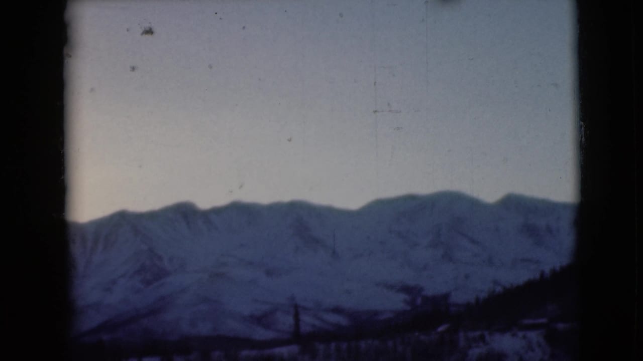 Snow-covered mountains seen through a dark window frame with pale sky above.