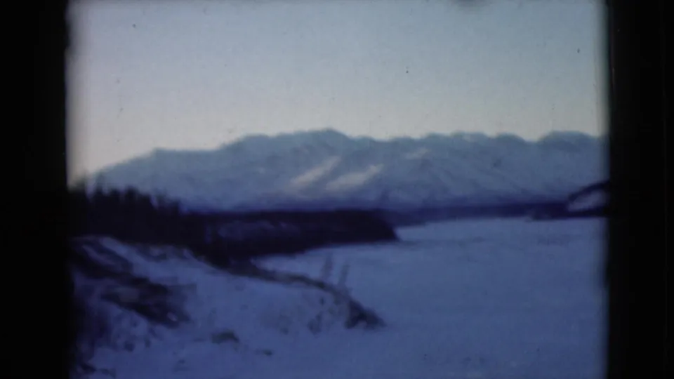 1946 Alaska 8mm frame showing snowy banks, a frozen waterway and distant mountains, with dark frame edges and soft grain.