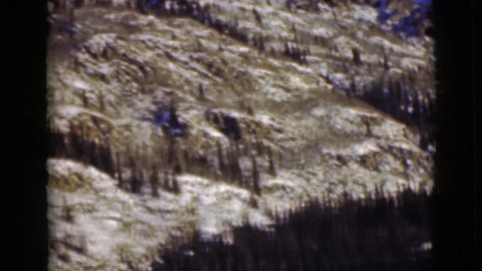 1946 Alaska 8mm frame showing a rugged snow-patched mountainside with dark evergreens across the lower slope.
