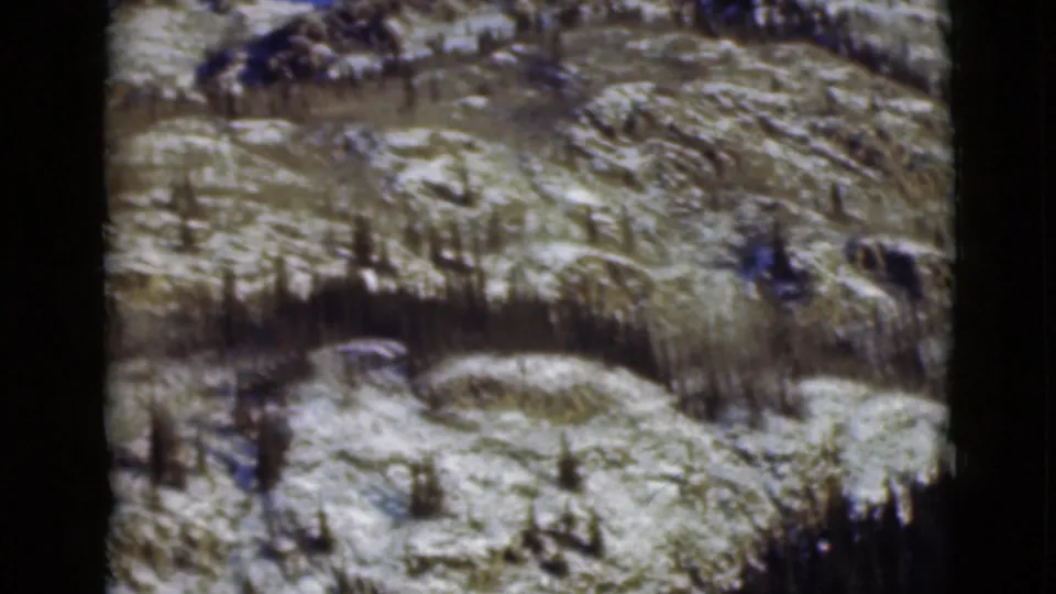 1946 Alaska home-movie frame of patchy snow across rocky terrain, with thin evergreen growth on the slope.