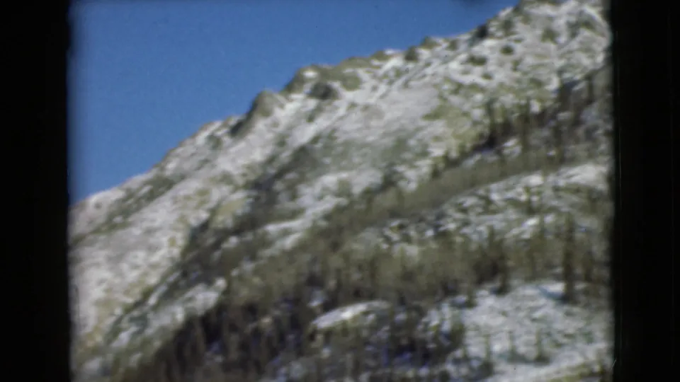 1946 Alaska 8mm view looking across a pale rocky ridge with snow patches and sparse trees near the lower edge.