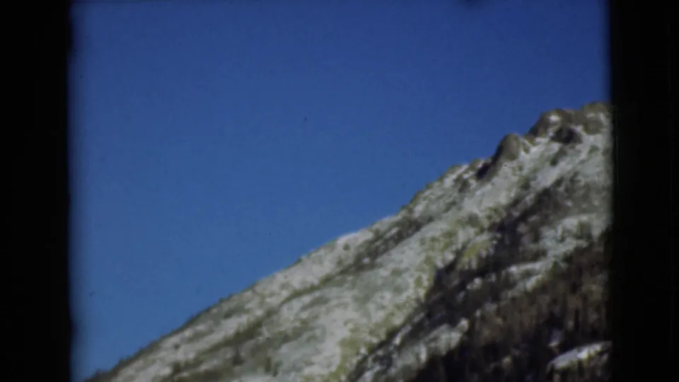 1946 Alaska frame with a rocky snow-patched ridge rising diagonally into a broad clear blue sky.