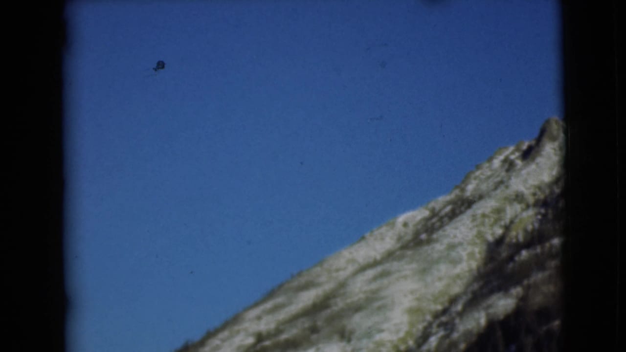 1946 Alaska 8mm frame showing a rugged mountain slope against clear blue sky with visible film edges.
