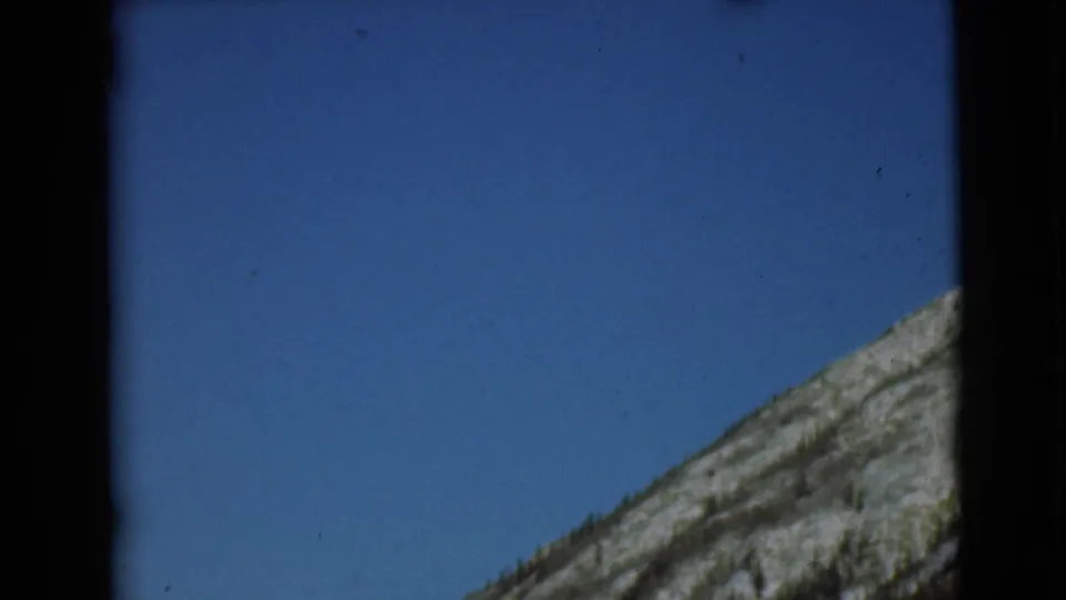 1946 Alaska 8mm frame with a sloping rocky hillside entering from the right under clear sky.