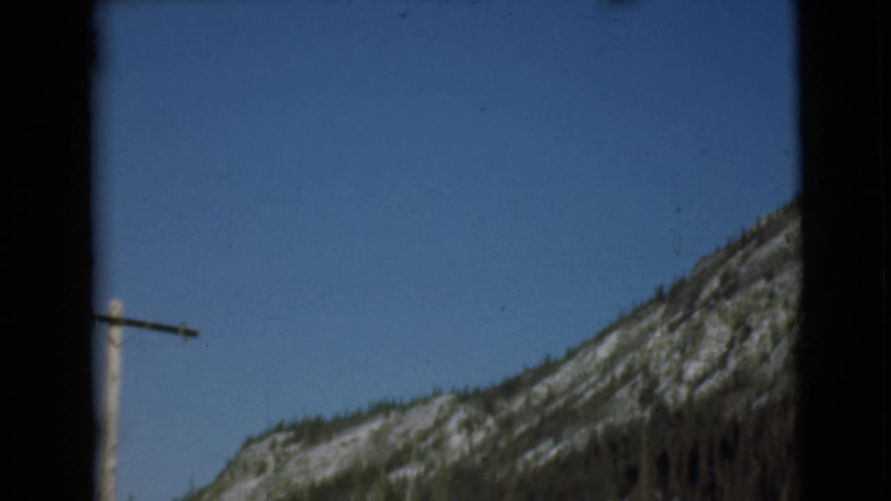 Telephone pole beside snow-streaked mountains under a blue sky.