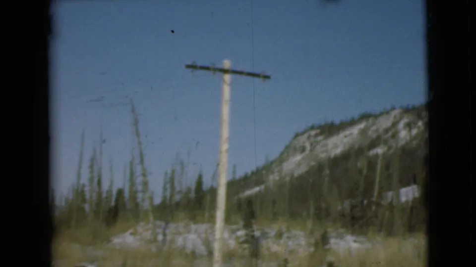 1946 Alaska 8mm view of a telephone pole, sparse evergreens, dry grass, and a snow-marked mountain slope.
