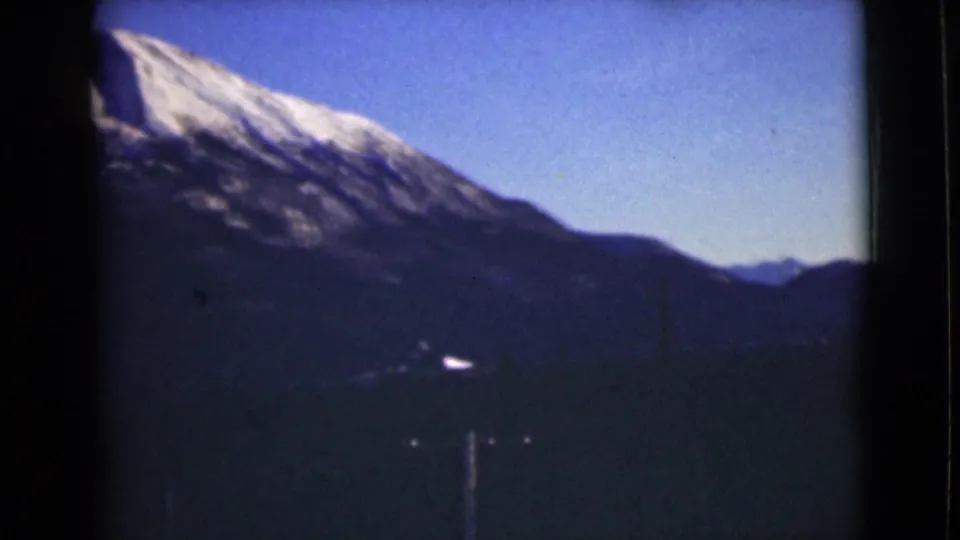 1946 Alaska 8mm frame showing a bright snow-covered peak above dark mountain slopes, with a small pale shape in the valley area.