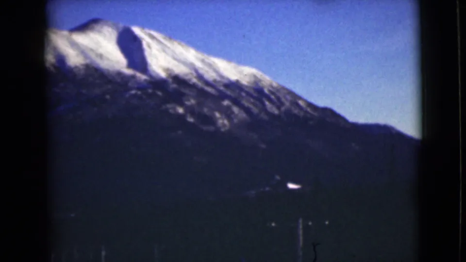 1946 Alaska home-movie view of a snow-covered mountain crest, dark foreground terrain, and faint vertical telephone poles near the lower frame.