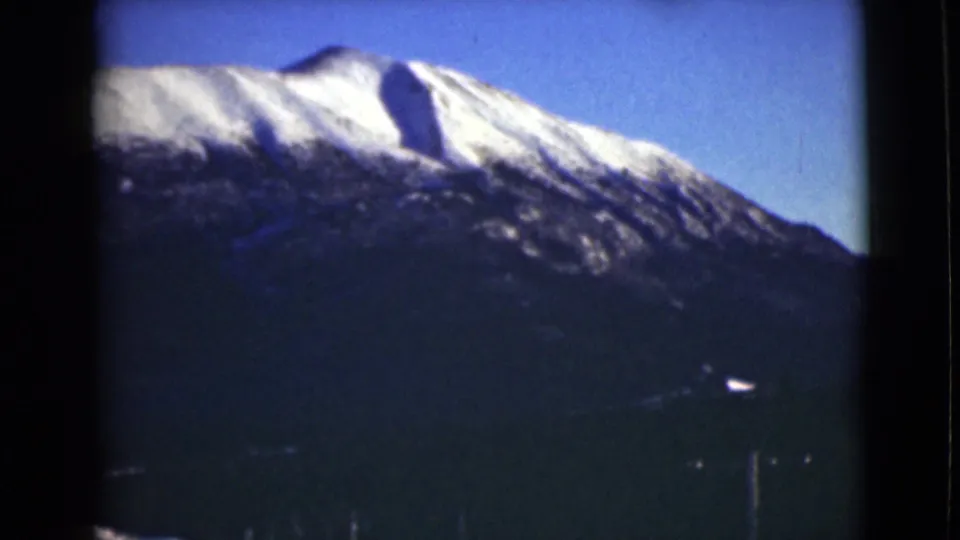 1946 Alaska 8mm still of a bright snow-capped ridge over dark slopes, with faint roadside telephone poles and film border visible.