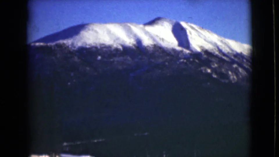 1946 Alaska home-movie frame of a bright snow-covered ridge over a dark mountain slope under blue sky.