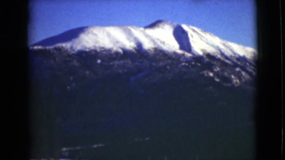 1946 Alaska 8mm frame with the snowy upper mountain filling more of the view above a dark forested base.