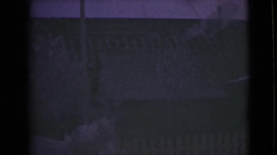 1946 Alaska frame showing a dim fence line, shrubs, and a pale curb or walkway, softened by grain and low exposure.