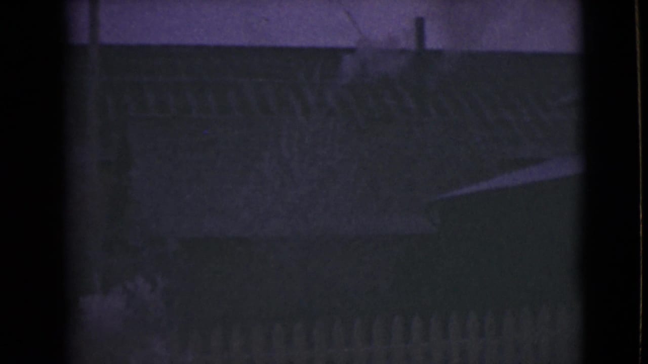Dark house roofline and picket fence under a purple night sky.