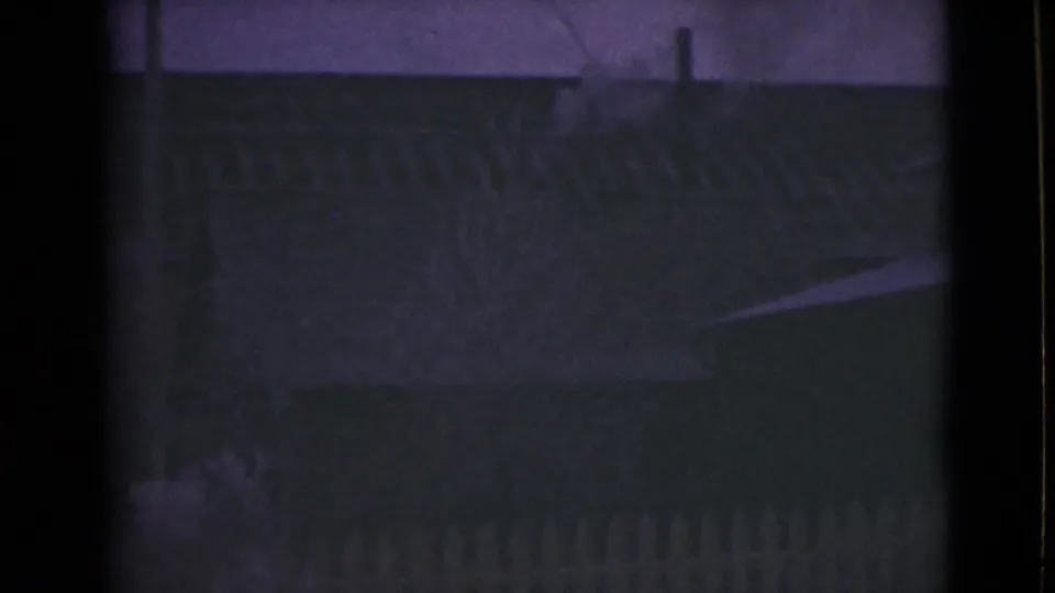 1946 Alaska 8mm frame showing a dim house exterior with roofline, fence, and pale ground in low light.