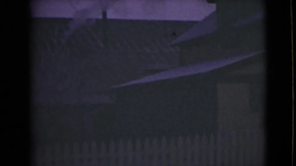 Low-light 8mm view of an Alaska house exterior, with roof eaves and fence barely visible against the sky.