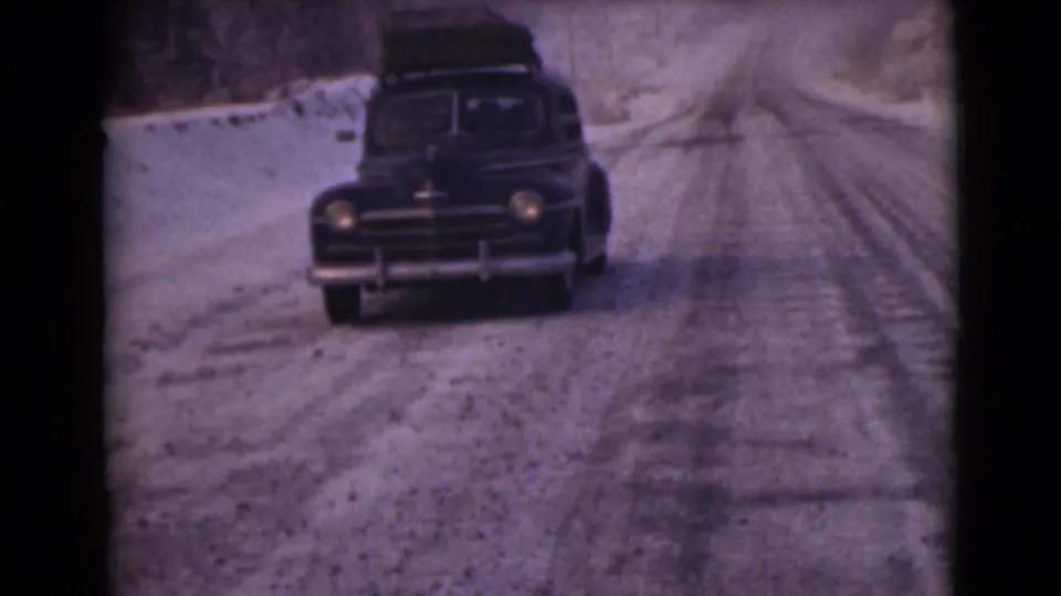 A 1946 Alaska 8mm frame shows a dark sedan with roof luggage approaching on a snow-covered rural road.