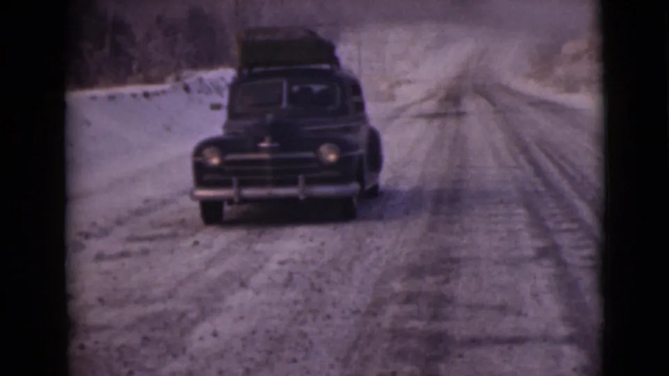 A closer 1946 Alaska frame shows the dark sedan and roof luggage advancing over tracked snow.
