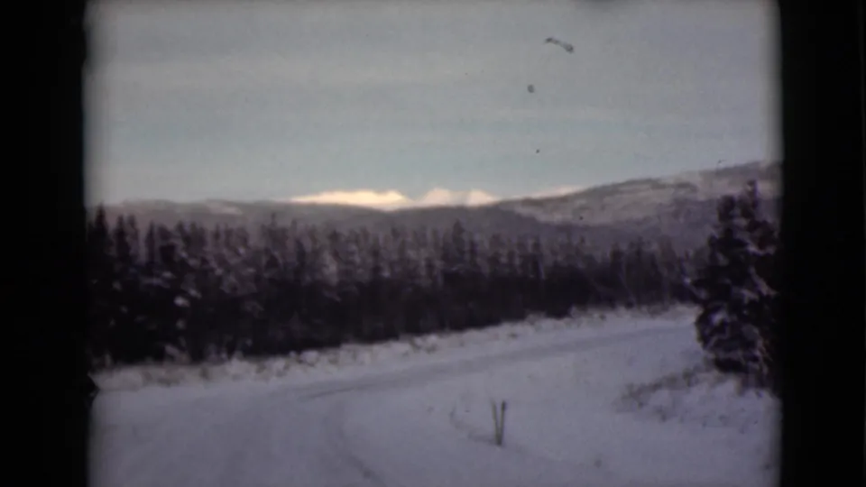 1946 Alaska 8mm view of a snow-blanketed road or field, dark forest, and distant winter mountains.