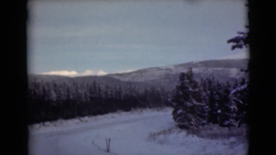 1946 Alaska 8mm frame with a snow road, dark conifers, distant mountains, and visible home-movie softness and grain.