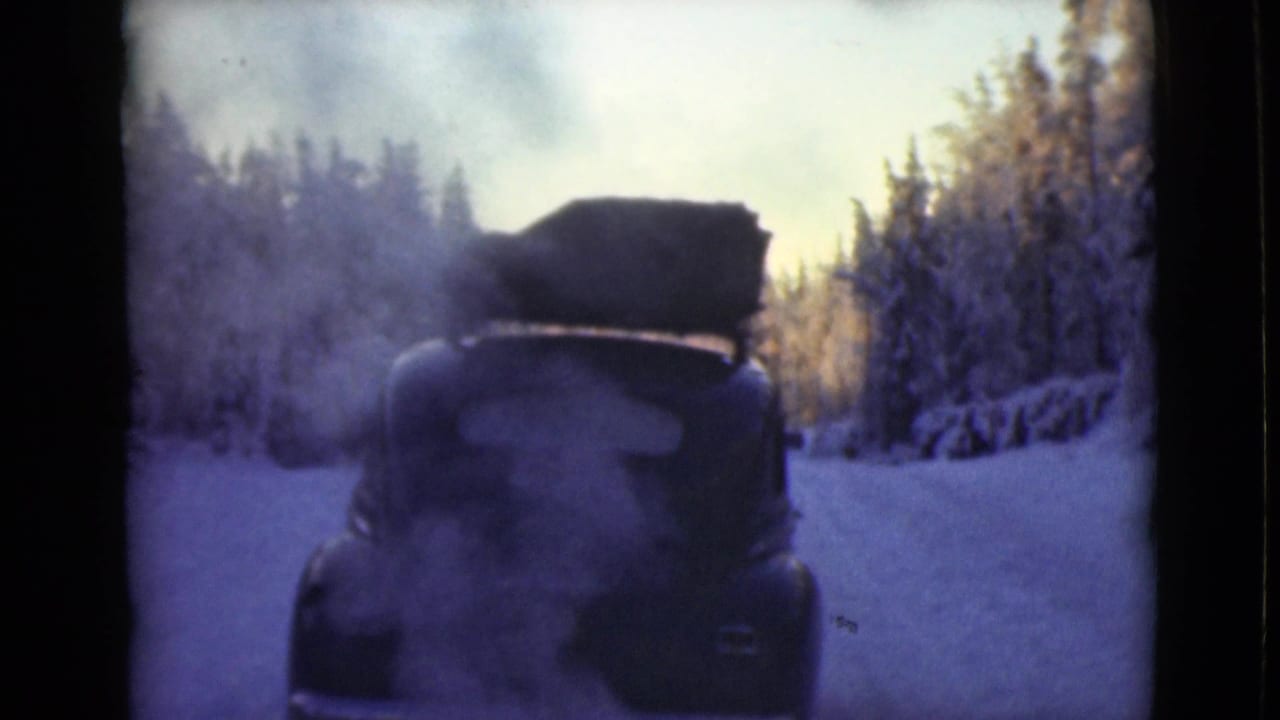 Smoking car with roof luggage stopped on a snowy forest road.
