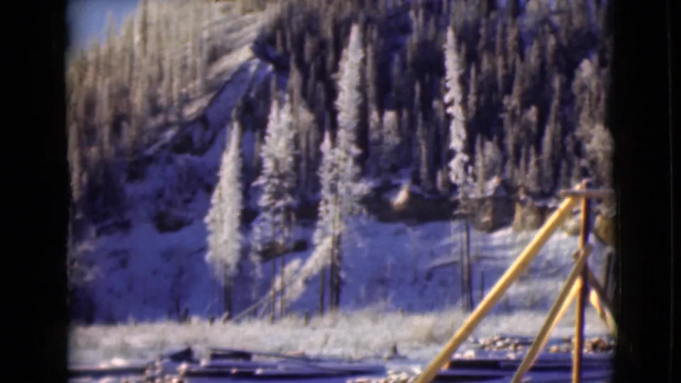 1946 Alaska mountain landscape with snow banks, frosted evergreens, and a yellow wooden railing or support in front.