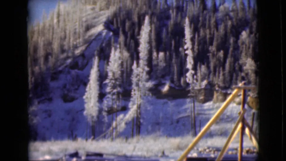 1946 Alaska 8mm frame showing a snowy mountain slope, frosted evergreens, and a wooden railing near the camera.