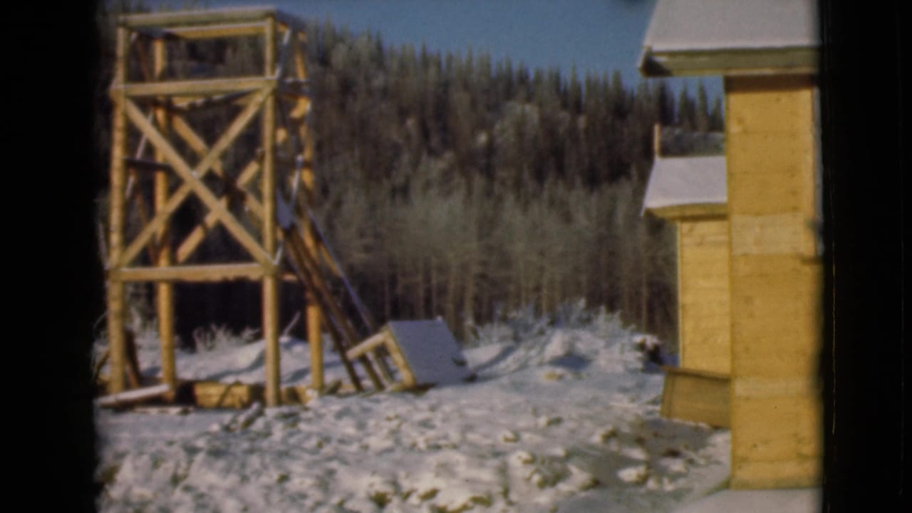 Wooden watchtower and cabin edge in a snowy forest clearing.