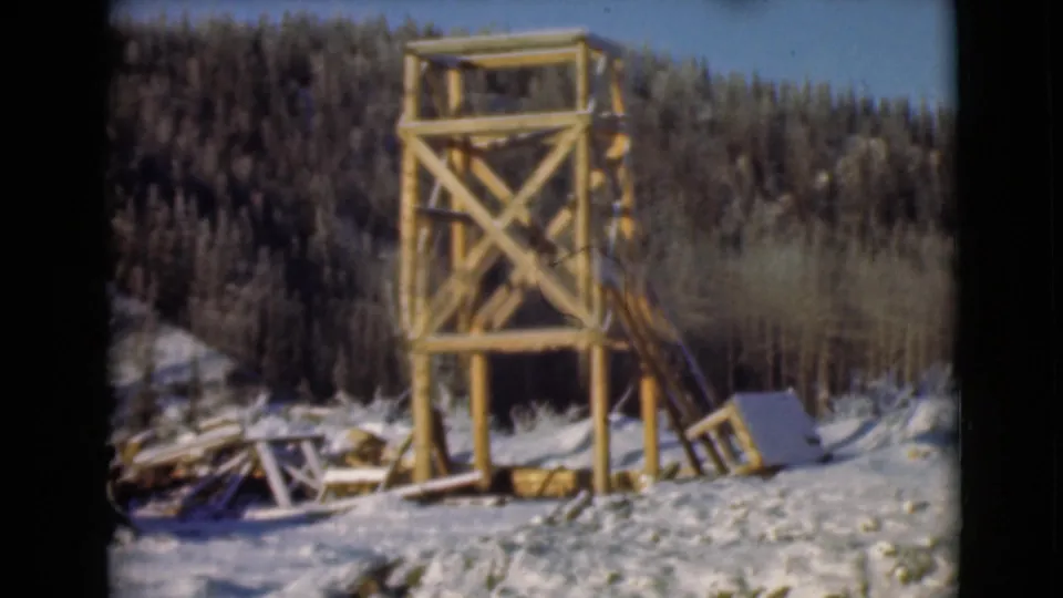 1946 Alaska 8mm frame with a wooden watchtower in a snowy clearing, backed by dense evergreen forest.