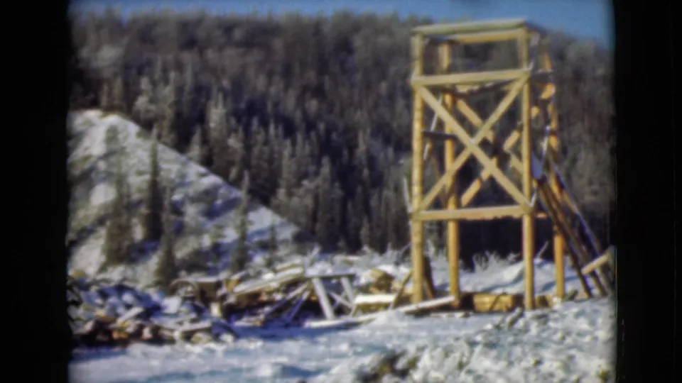 1946 Alaska 8mm frame showing the watchtower beside a snowy hillside with dark evergreen forest and cut lumber.
