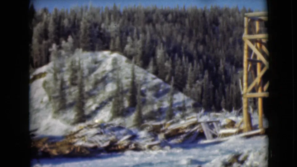 1946 Alaska 8mm frame with a snow-covered hillside, evergreen forest, scattered lumber, and the edge of a timber tower.