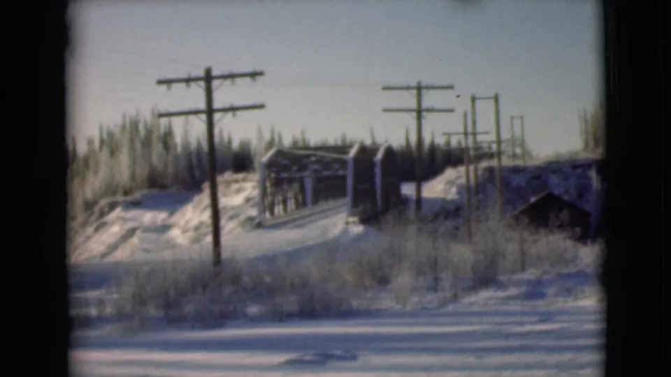1946 Alaska 8mm frame showing a snow-covered roadside with wooden utility poles, winter brush, and a small bridge or trestle.