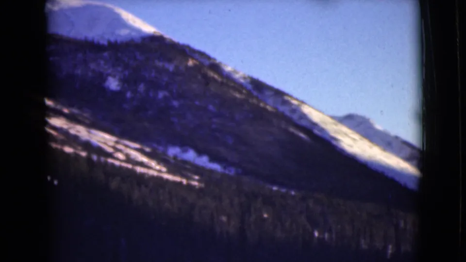 1946 Alaska 8mm frame showing a snow-bright ridge, shadowed forest below, distant mountains, and visible film borders.