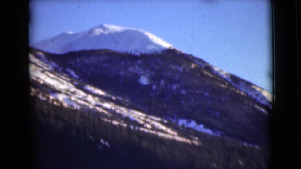 Archival 8mm view of an Alaska mountain with snow along the ridge and evergreen forest across the lower slope.
