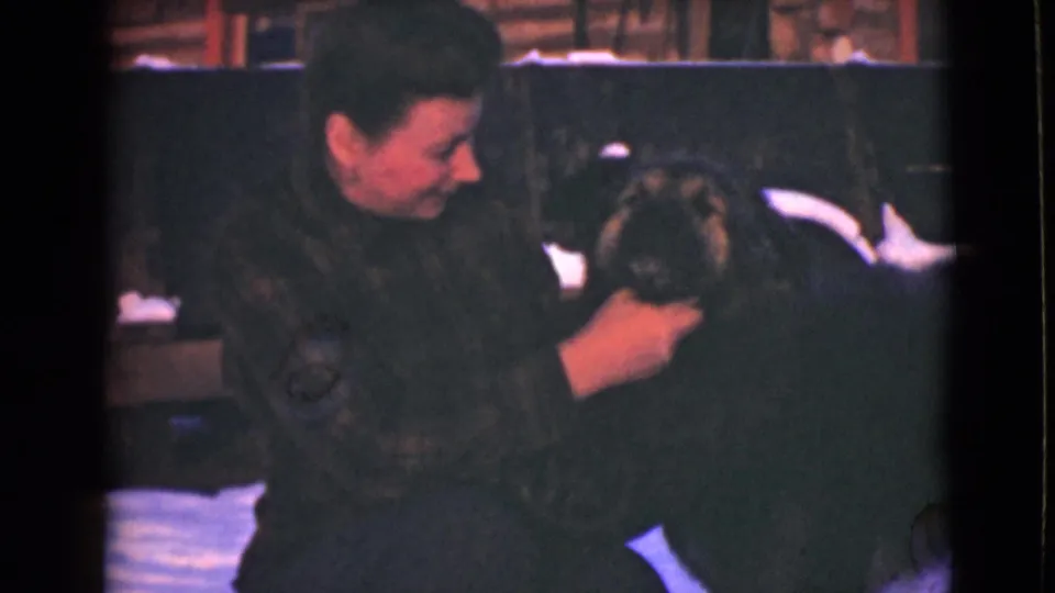 A closer 1946 Alaska frame shows the woman leaning toward the large dark dog, holding its head during an affectionate snowy outdoor moment.