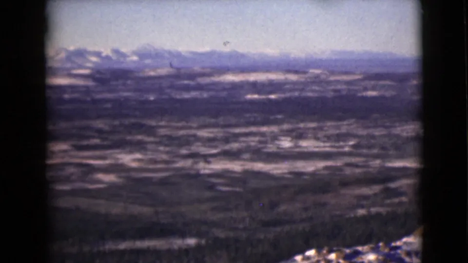 A wide 1946 Alaska home-movie view shows snowy terrain, dark forested areas, and a mountain range across the horizon.