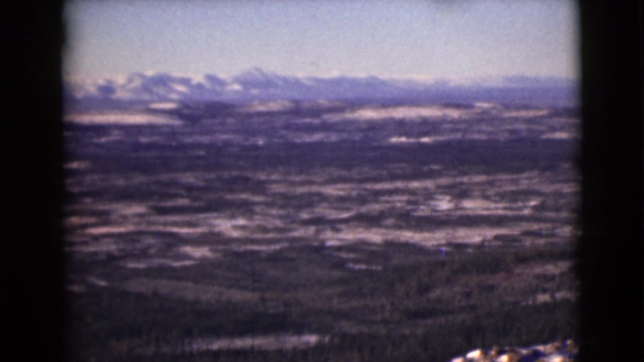 1946 8mm Alaska home-movie frame showing a distant snowy mountain range beyond a wide valley and forested hills.