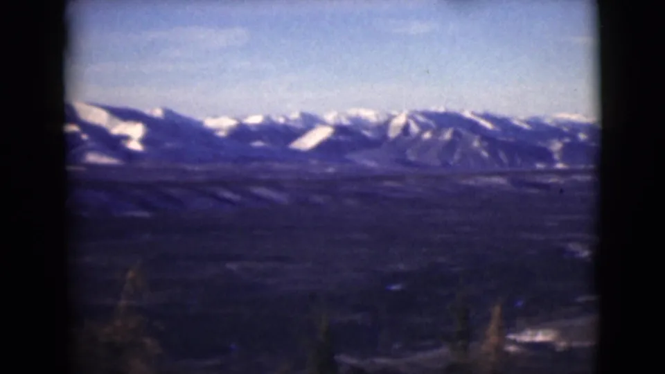 1946 Alaska 8mm frame with a mountain ridge, patches of snow, open valley floor, and blue sky.
