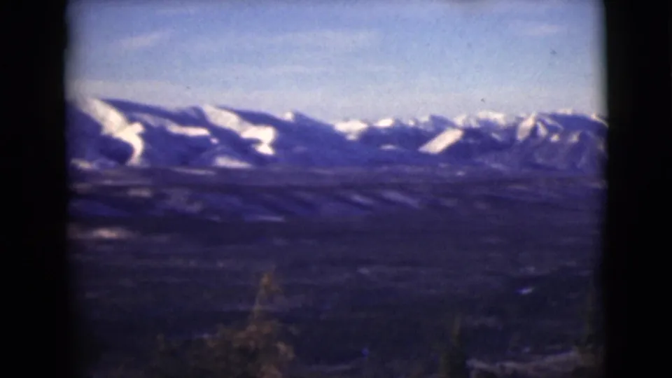 1946 Alaska 8mm frame showing snow-striped mountain slopes, a broad valley, and soft evergreen silhouettes.