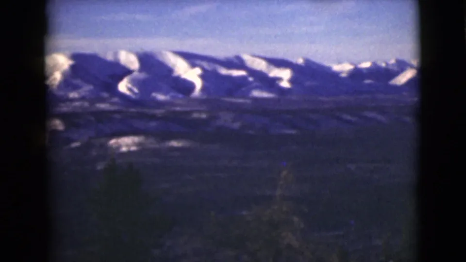 1946 Alaska 8mm frame of bright snowfields on distant mountains, with a dark valley and trees below.