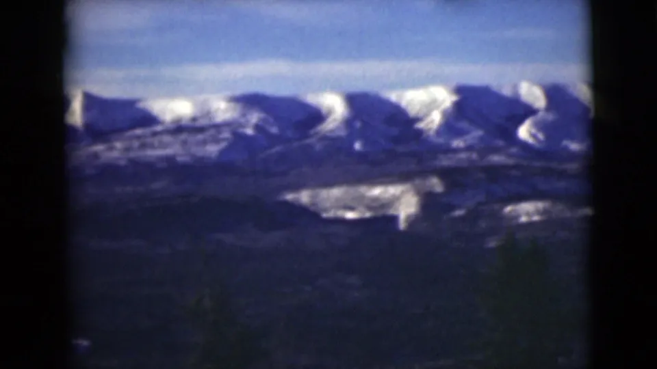 1946 Alaska home-movie frame showing a broad snowy mountain range beyond dark foreground land.