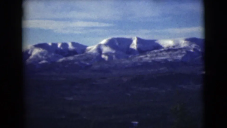 1946 Alaska home-movie frame showing snow-dusted peaks, dark lower terrain, and blue sky at the end of the pan.