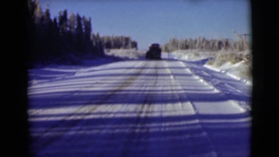 1946 Alaska 8mm frame from a moving road view, showing blue shadows across snow and a vehicle in the distance.