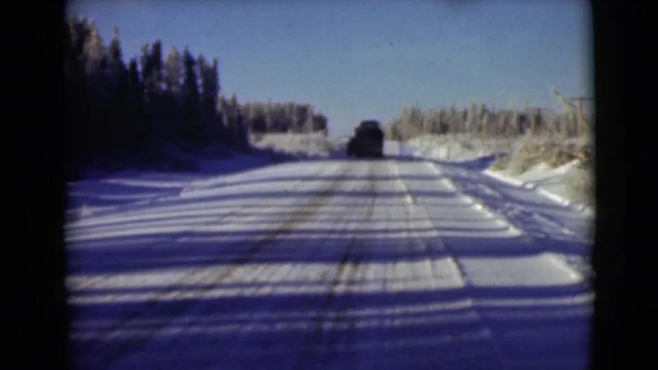 Mid-1940s Alaska home-movie frame of a vehicle continuing along a sunlit snowy road.